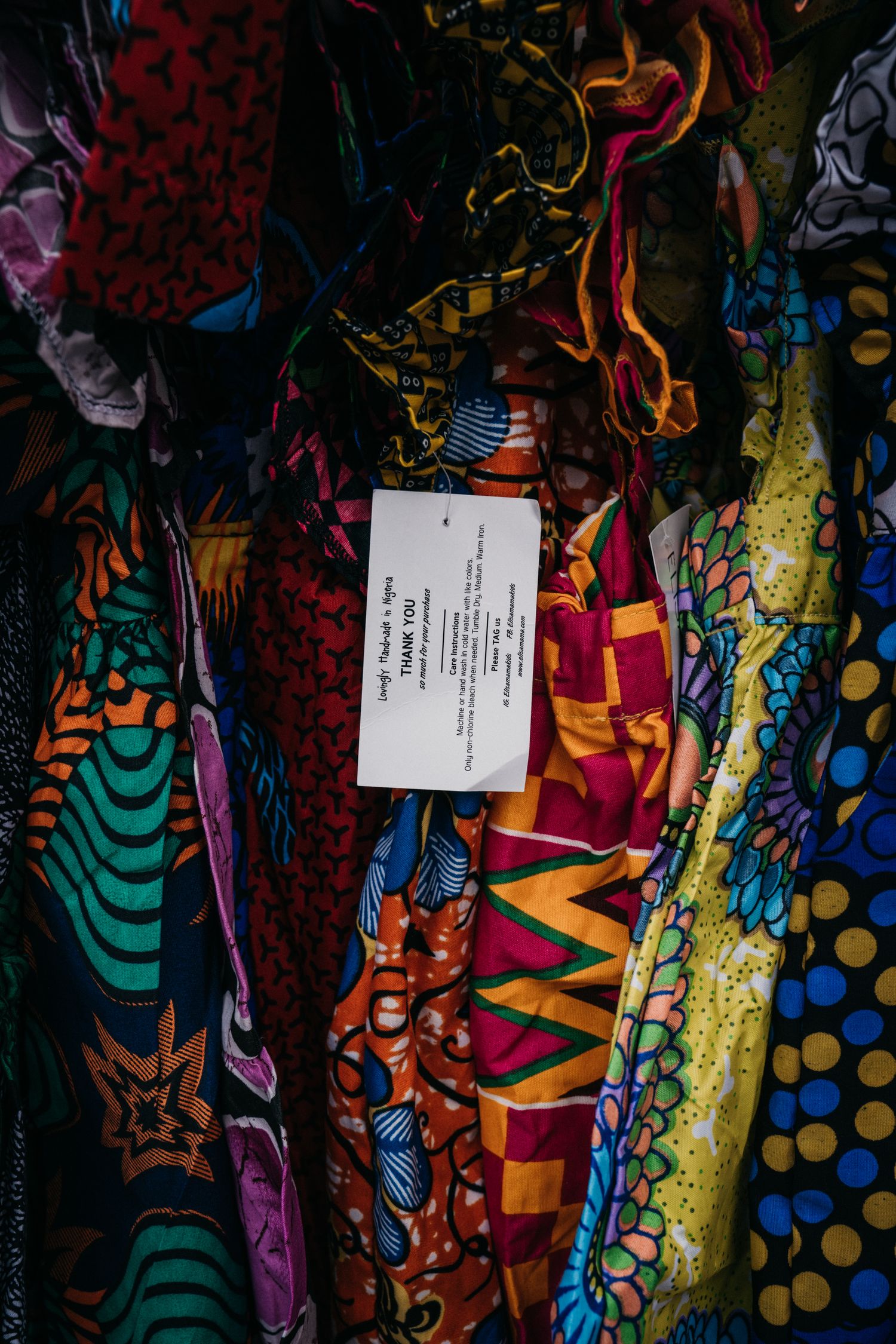 Colorful African print fabrics hanging on a rack with a price tag visible among vibrant patterns.