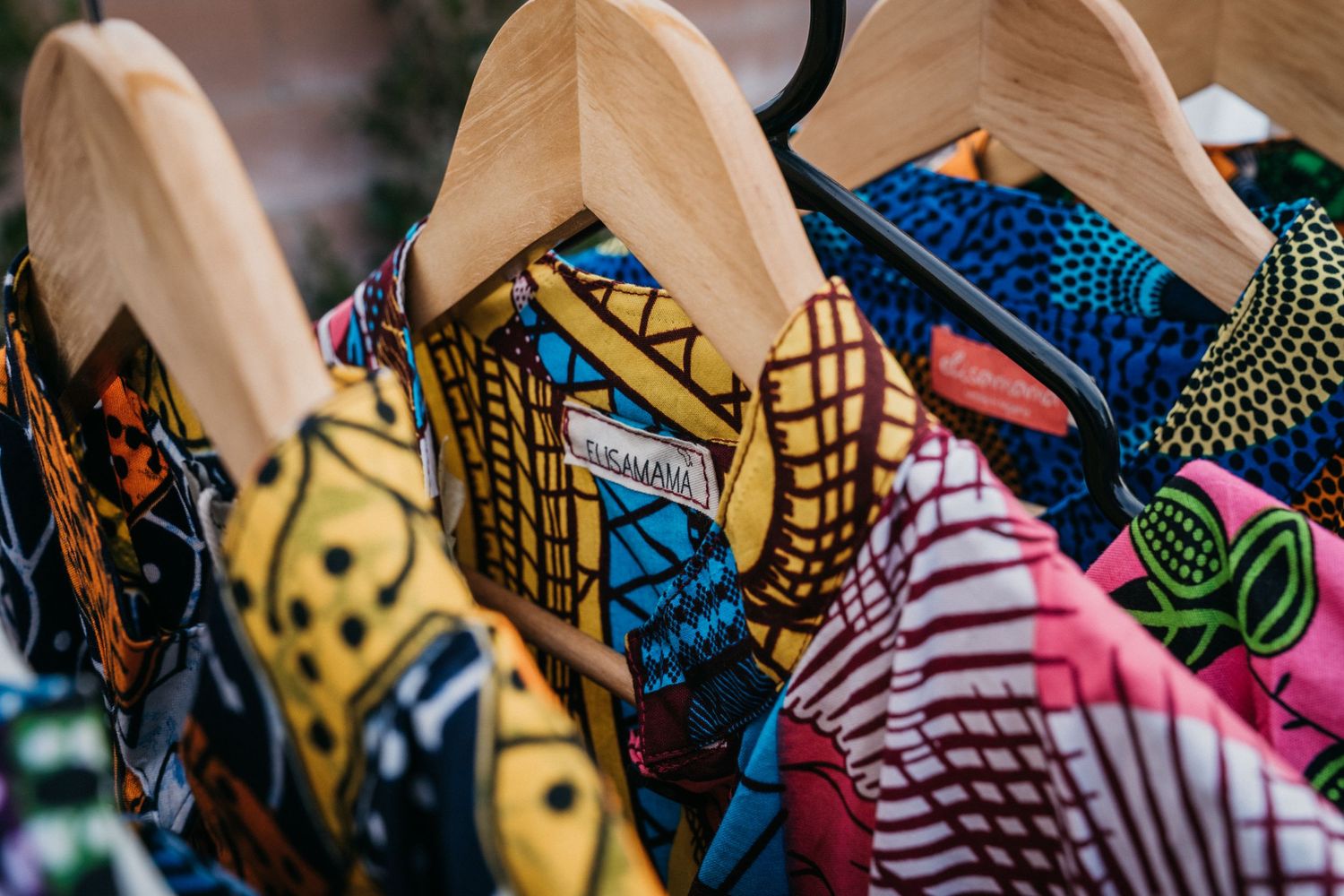 Colorful African print shirts on wooden hangers displayed at a market stall.
