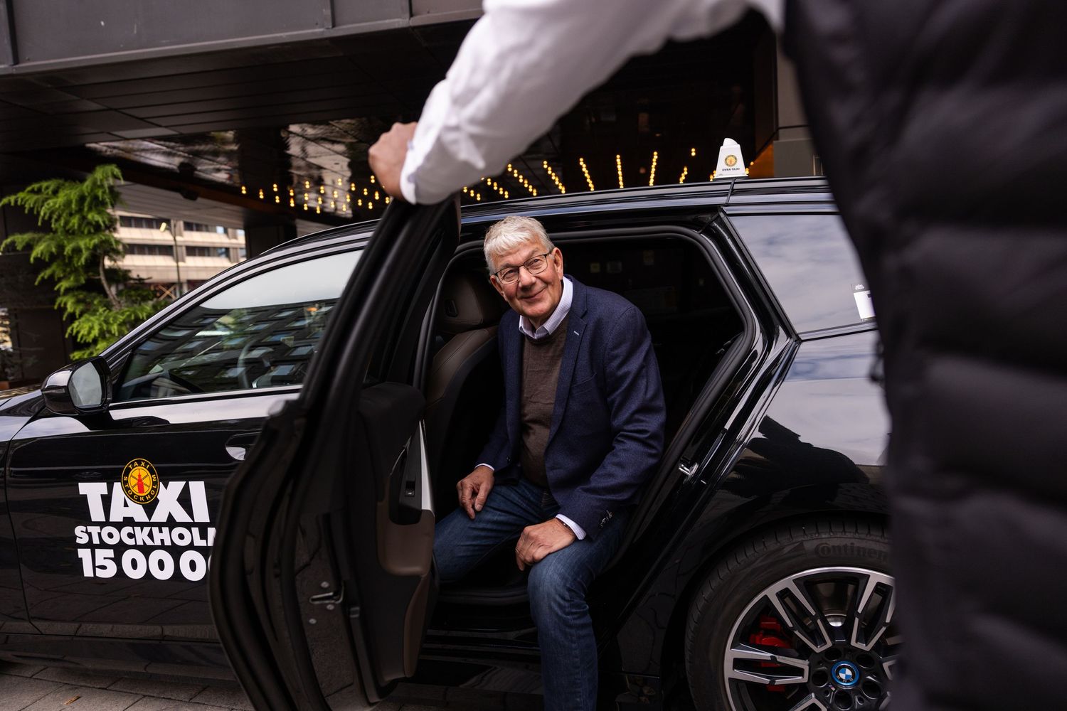 Press photo of a person stepping out of a taxi cab while someone opens the car door.