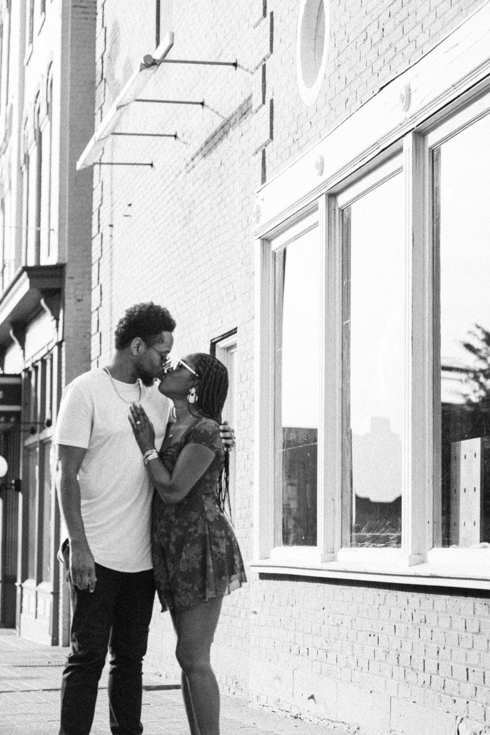Black and white photo of a couple sharing a romantic kiss on an Lexington Kentucky sidewalk beside a brick building.