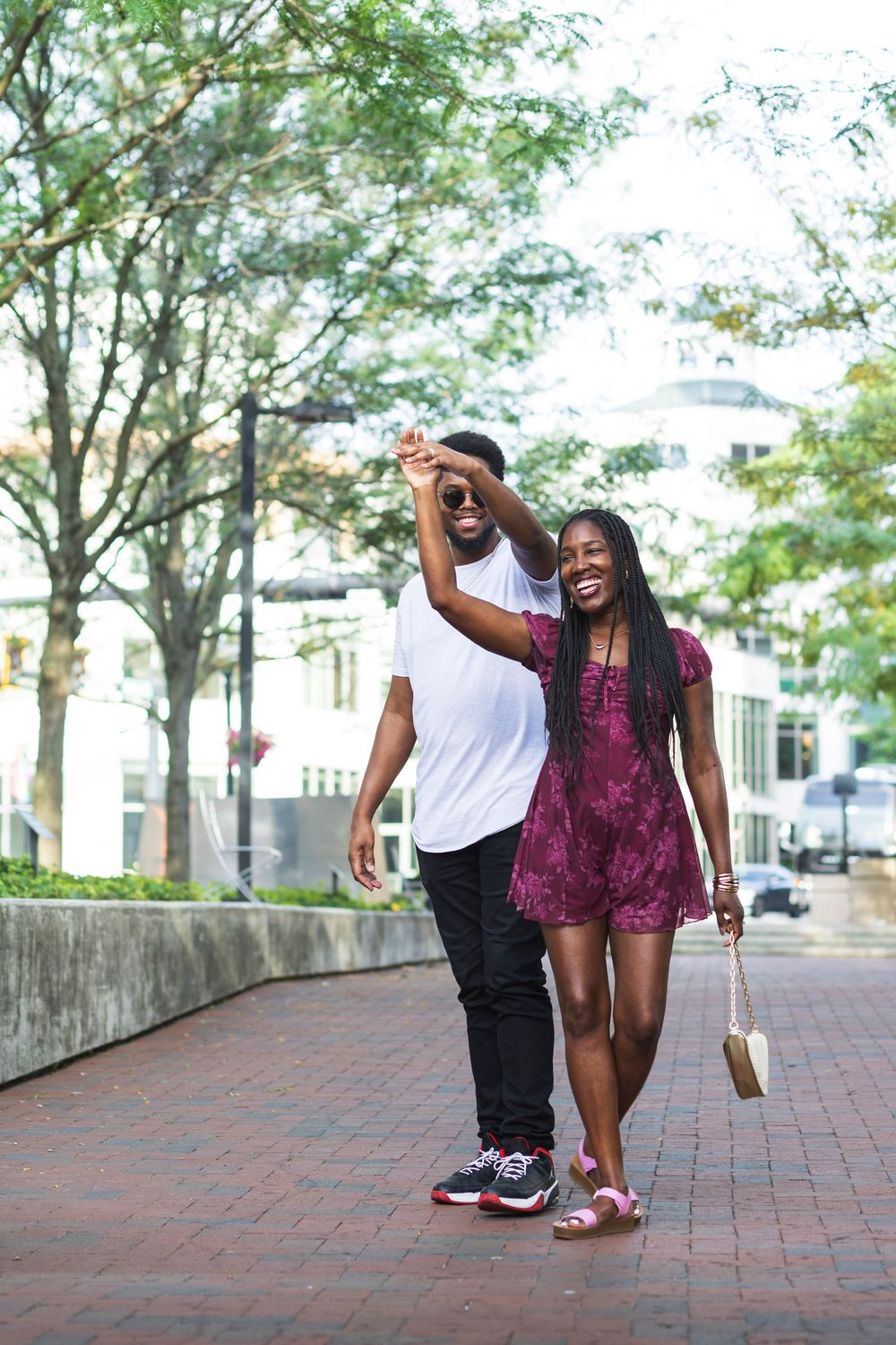 A joyful couple dancing together on a brick walkway surrounded by lush green trees in Triangle Park in Lexington Kentucky.
