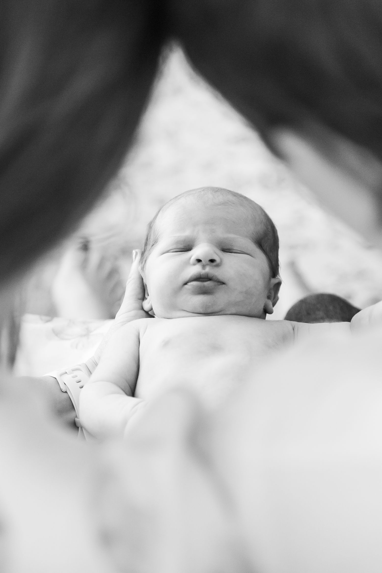 Black and white photo of a sleeping newborn baby being cradled in a parent's arms.