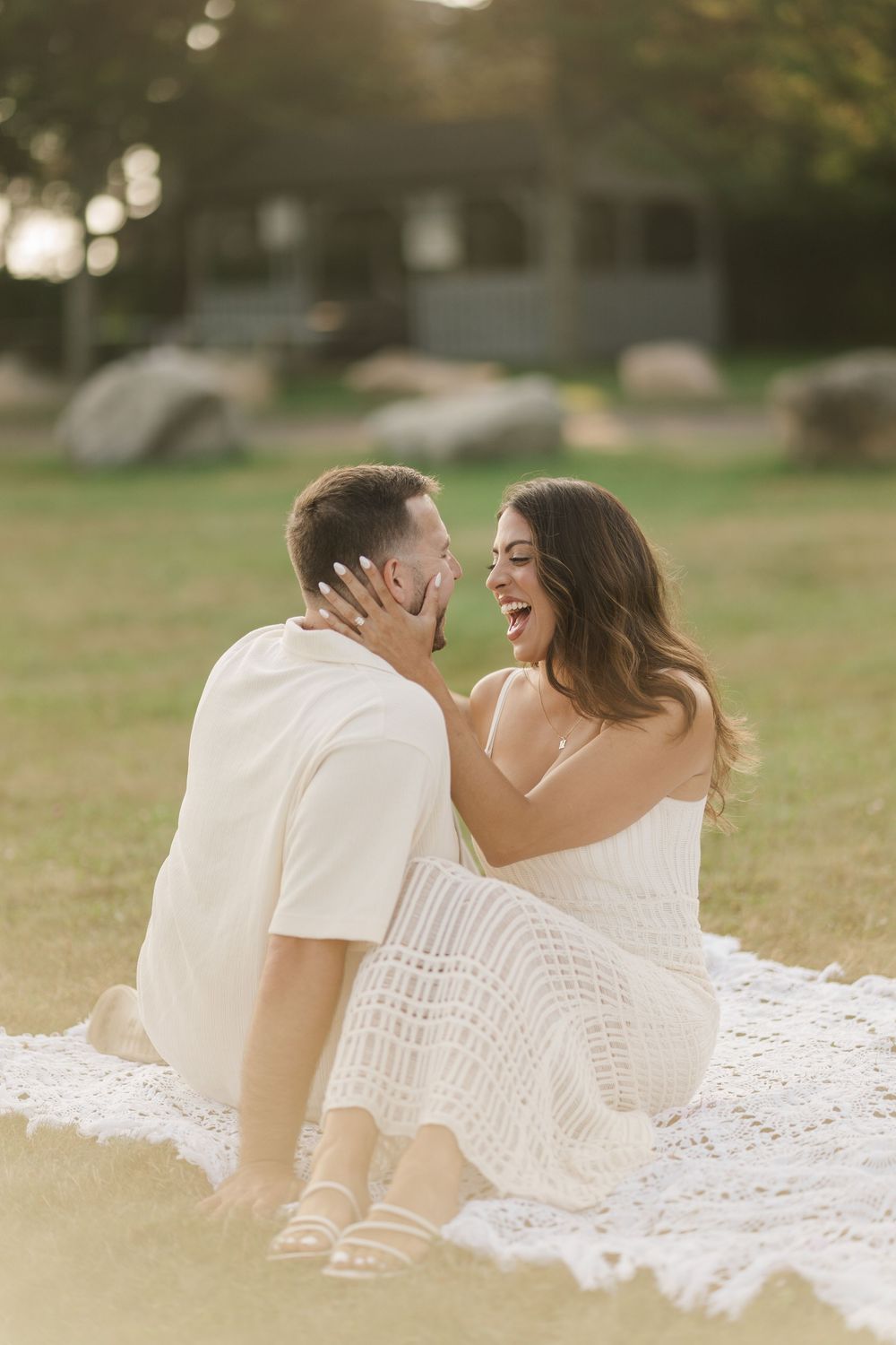 Happy couple laughing together on white blanket in sunny park during golden hour.