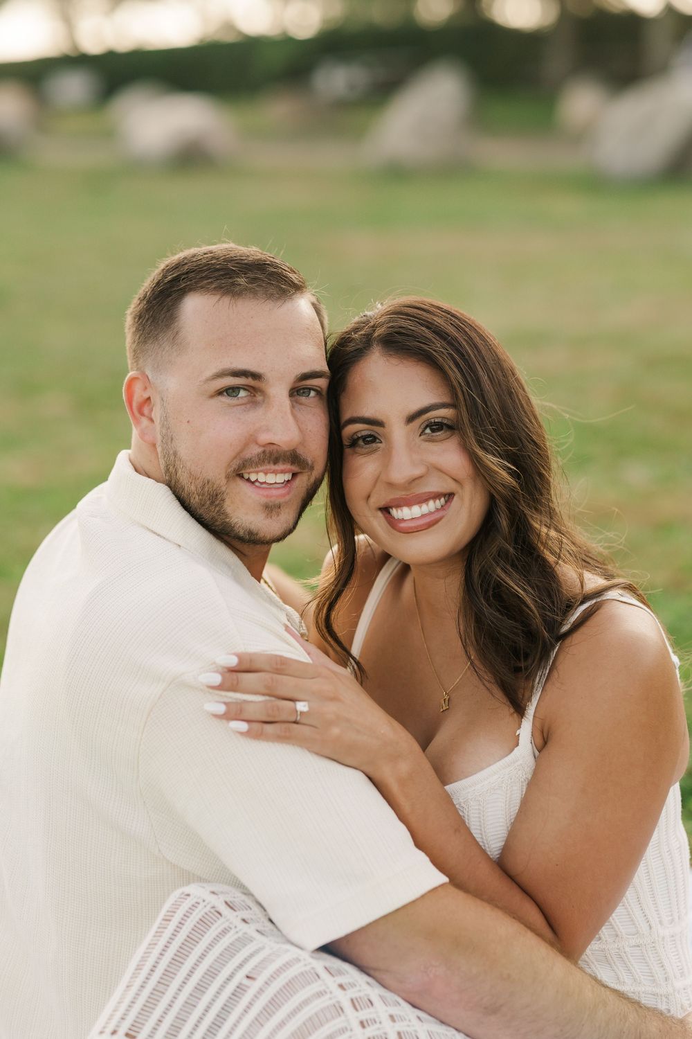 Smiling engaged couple embracing outdoors on grass during golden hour engagement photo session.