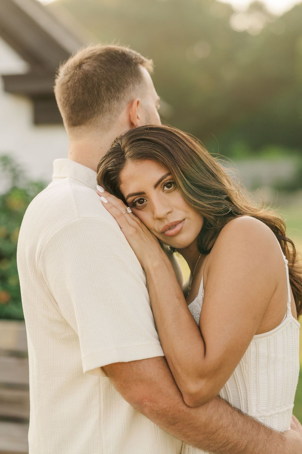 A woman in a white dress rests her head on a man's shoulder during a romantic outdoor couples photo session.