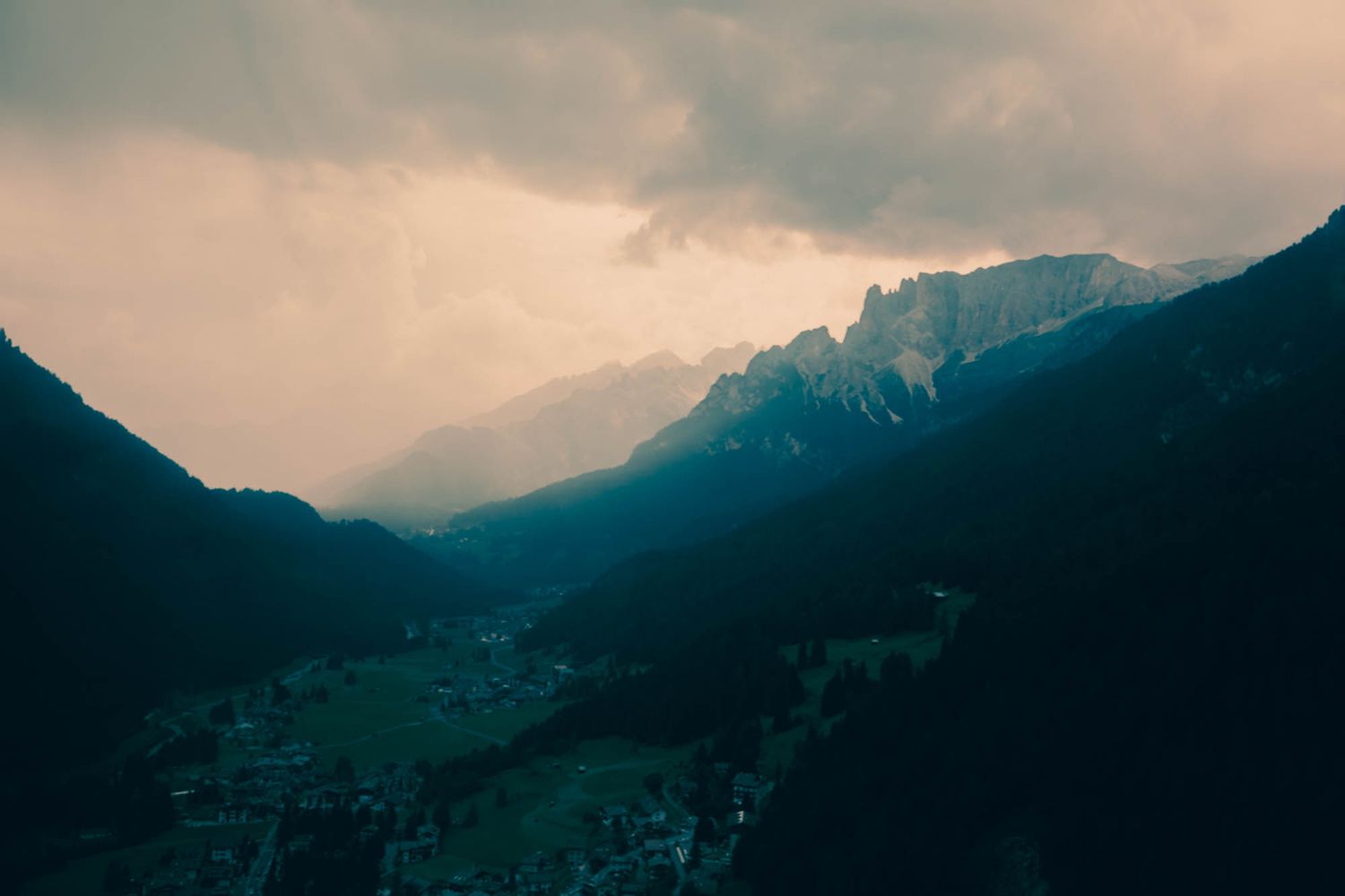 Dramatic Dolomite mountains with jagged rocky peaks, winding road, and moody overcast sky in the Italian Alps.