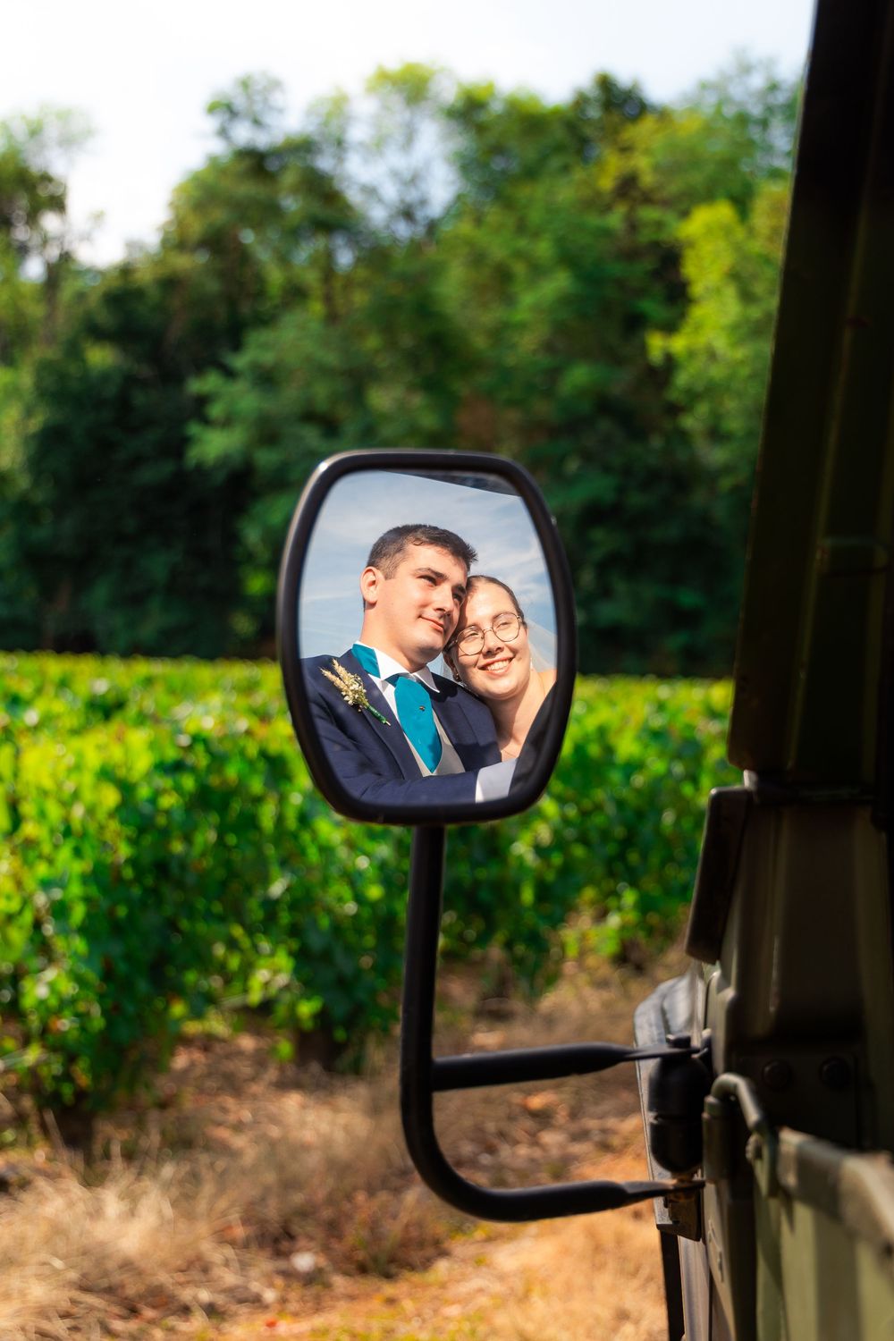 Couple smiling together reflected in a vintage vehicle side mirror with lush green vineyard background.