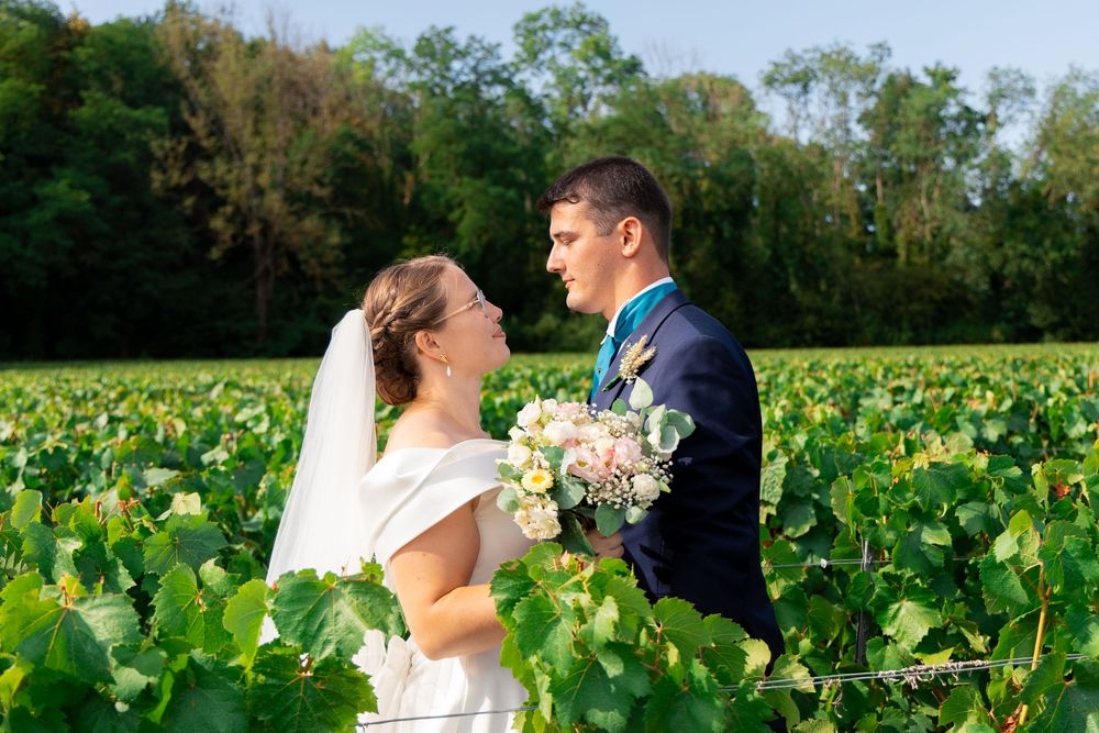 Bride and groom sharing a romantic moment in a lush vineyard, bride holding a bouquet on a sunny wedding day.
