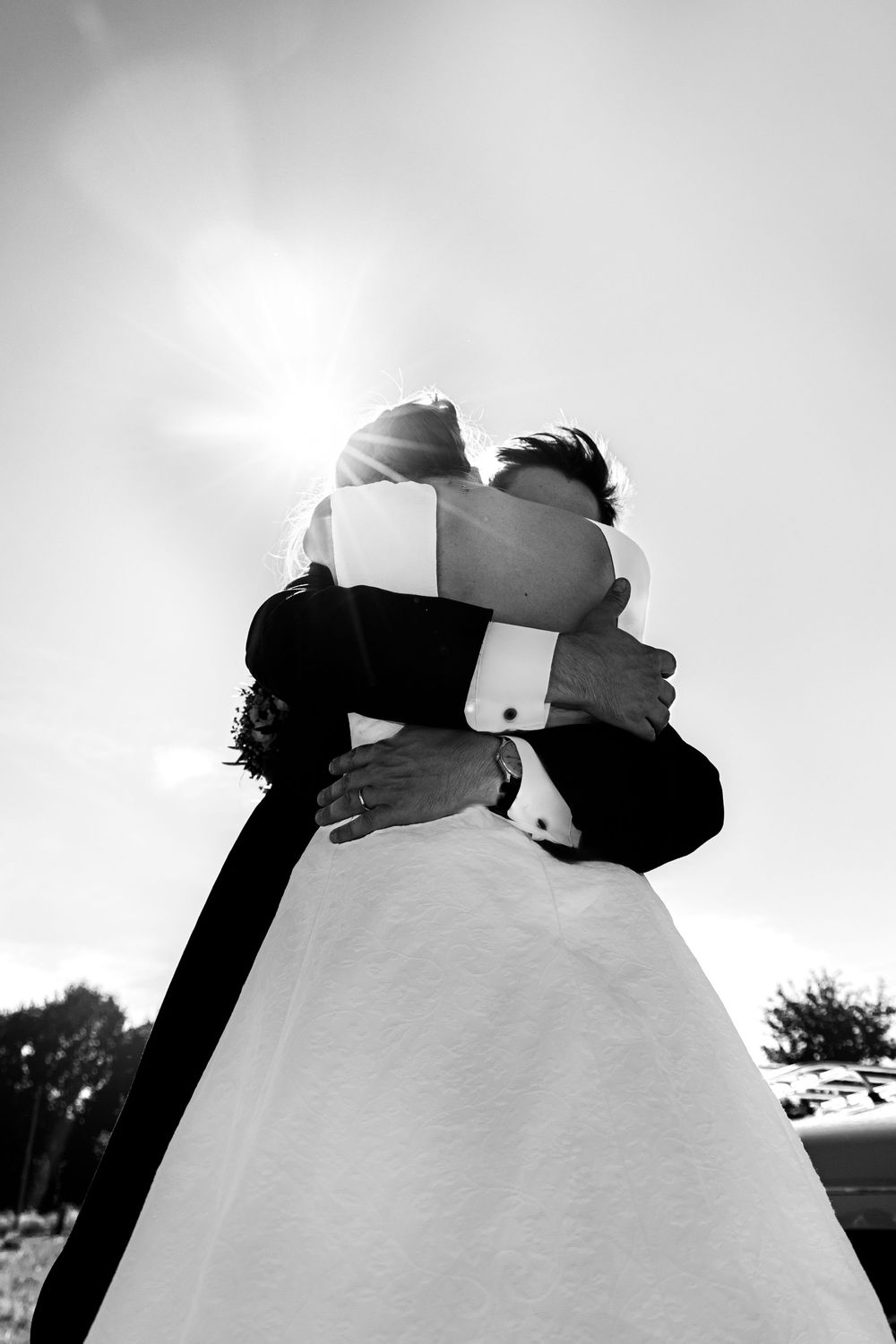 Black and white photo of bride and groom embracing under bright sunlight on their wedding day.