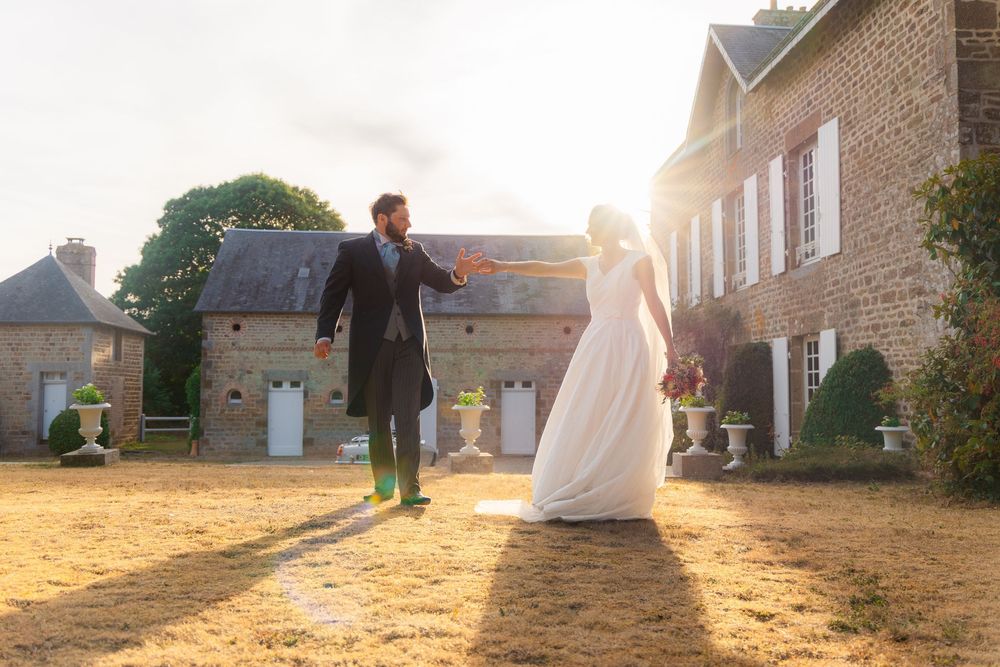 Bride and groom holding hands at golden hour outside a rustic stone manor house on their wedding day.