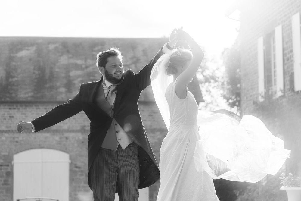 Black and white photo of a joyful bride and groom dancing outdoors on their wedding day.