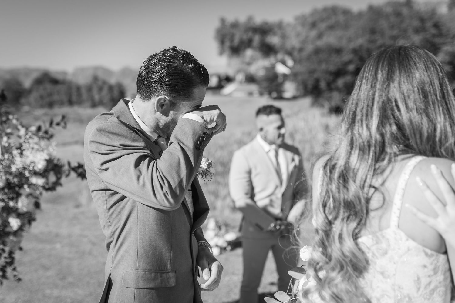 Emotional groom wiping tears during outdoor wedding ceremony in black and white photo.