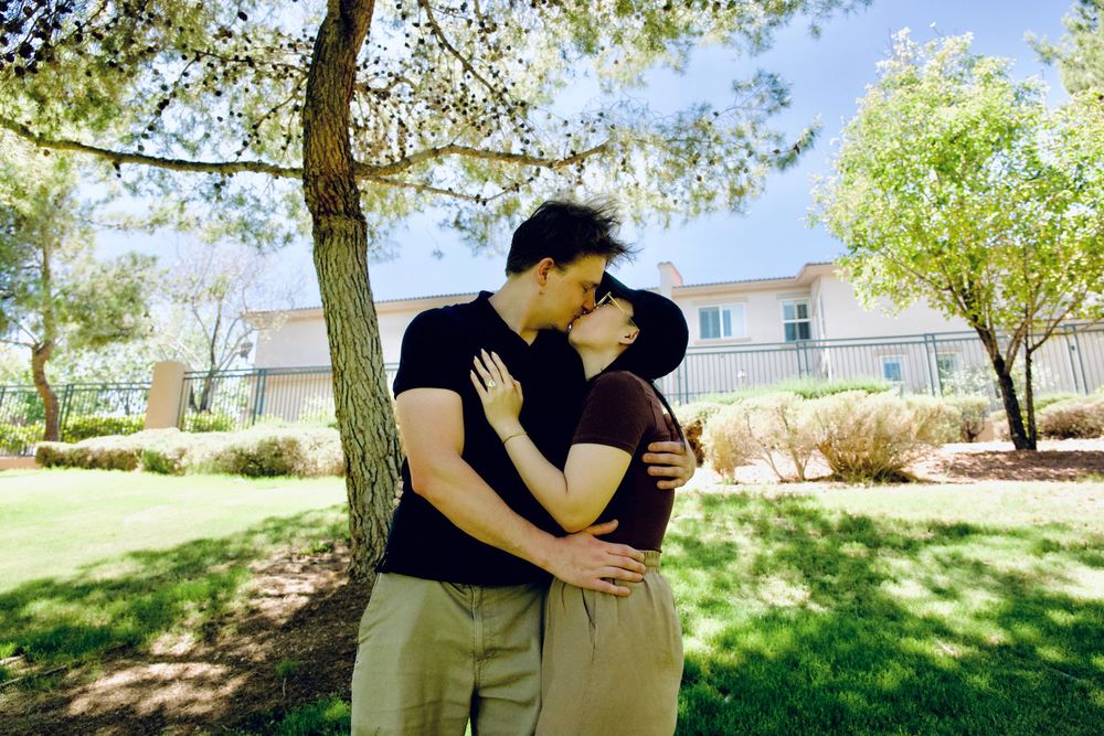 Romantic couple sharing a tender kiss under a blooming tree in a sunny green park.