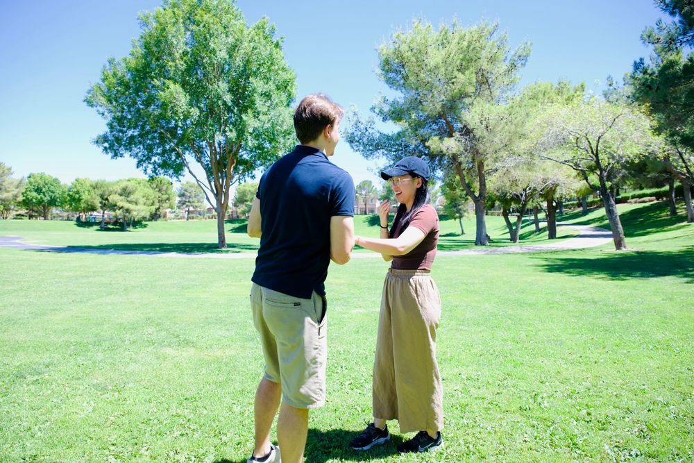 Couple holding hands and dancing together on lush green grass in a sunny park.