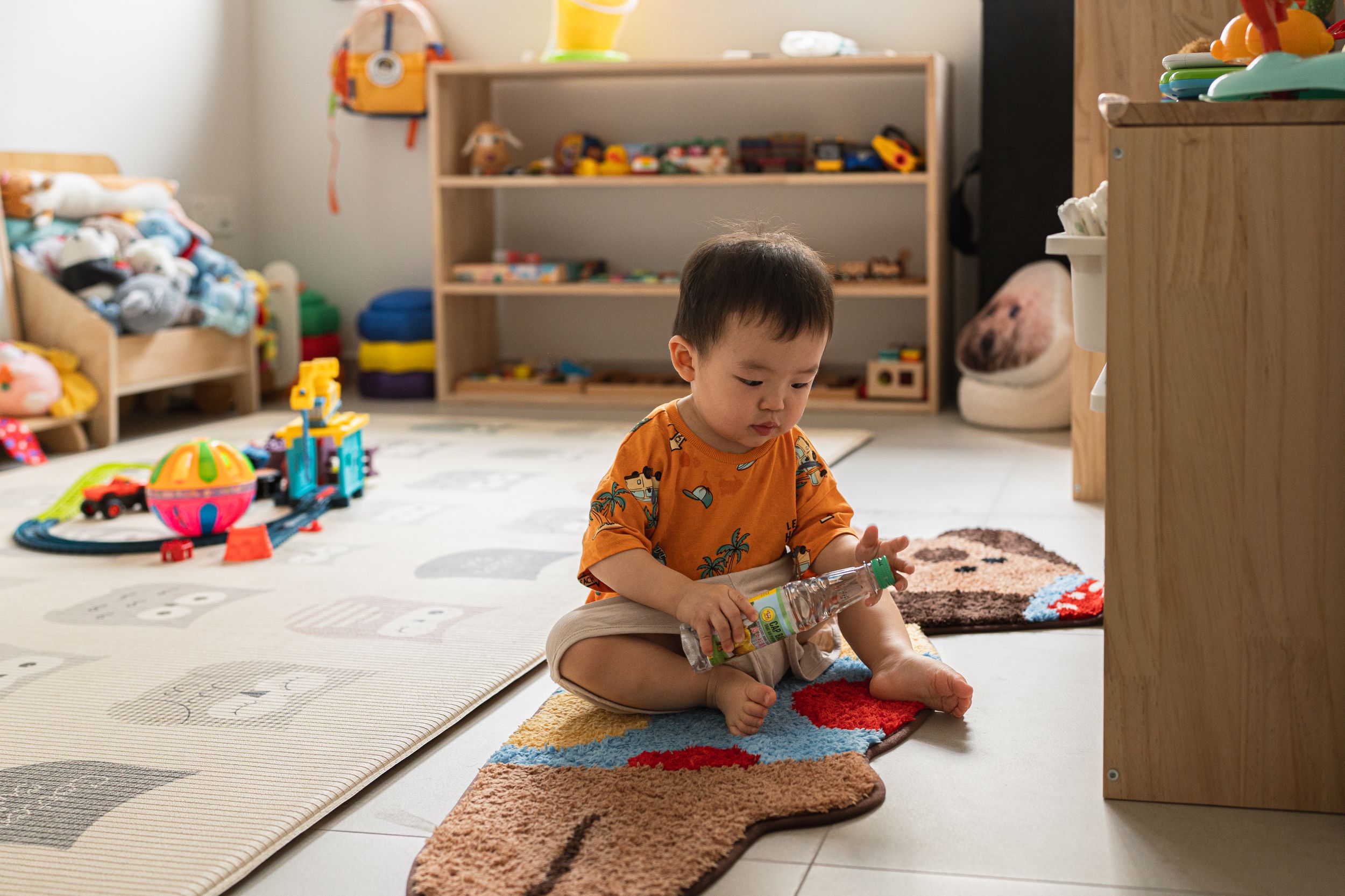 Child in orange shirt playing with toys on floor mat in playroom.