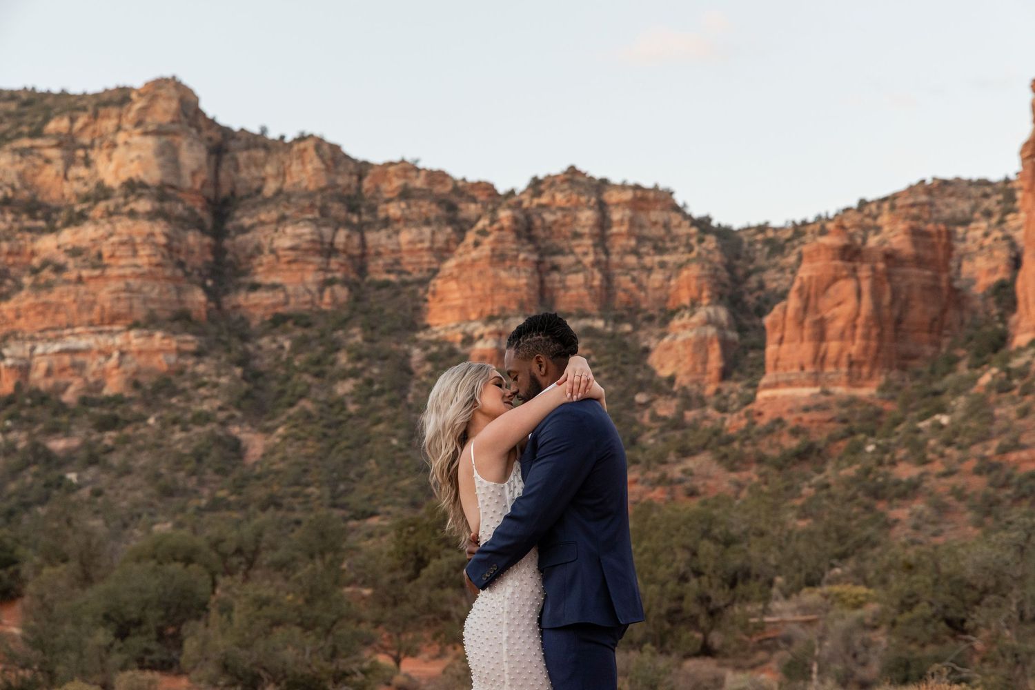 Couple embraces during sunset with majestic red rock cliffs of Sedona forming a dramatic backdrop in Arizona.