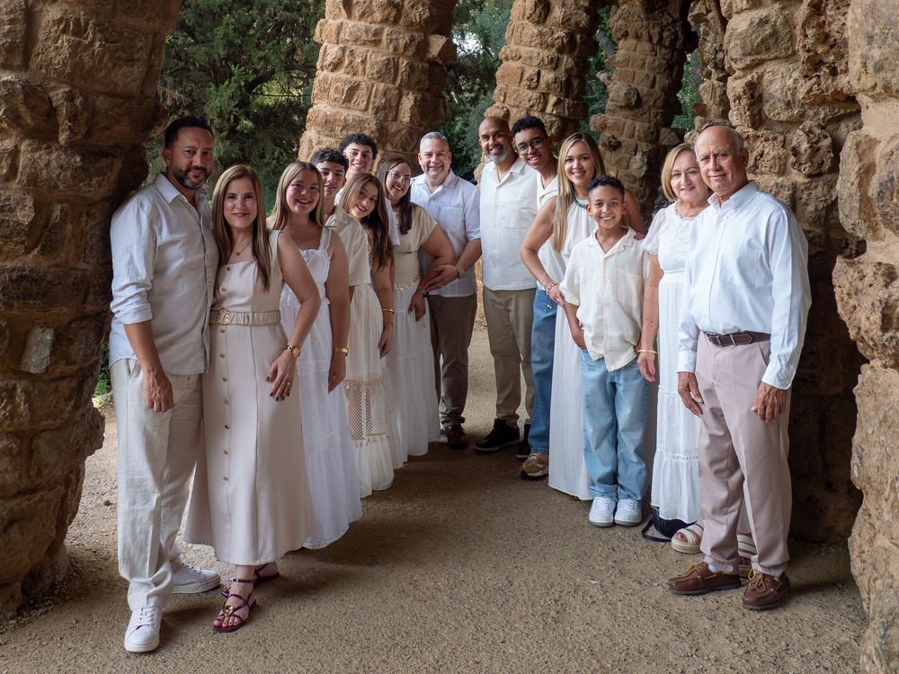 Group of people in white outfits posing together under stone arches at Park Guell, Barcelona.