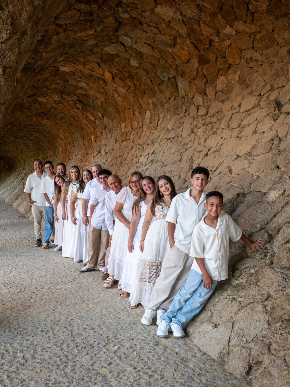 Large family group in white outfits posing in a stone tunnel archway at Park Güell, Barcelona.