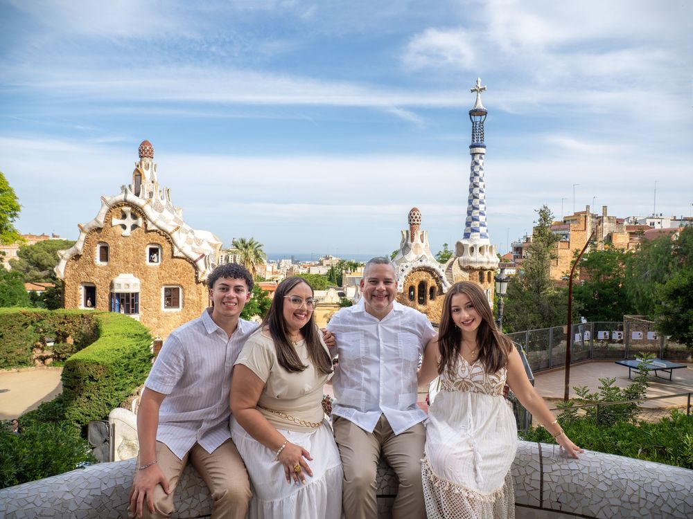 Four people pose smiling at Park Guell Barcelona with Gaudi architecture and city views behind them.