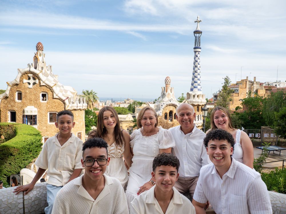 Family group photo at Park Güell Barcelona with Gaudí architecture and city skyline in background.