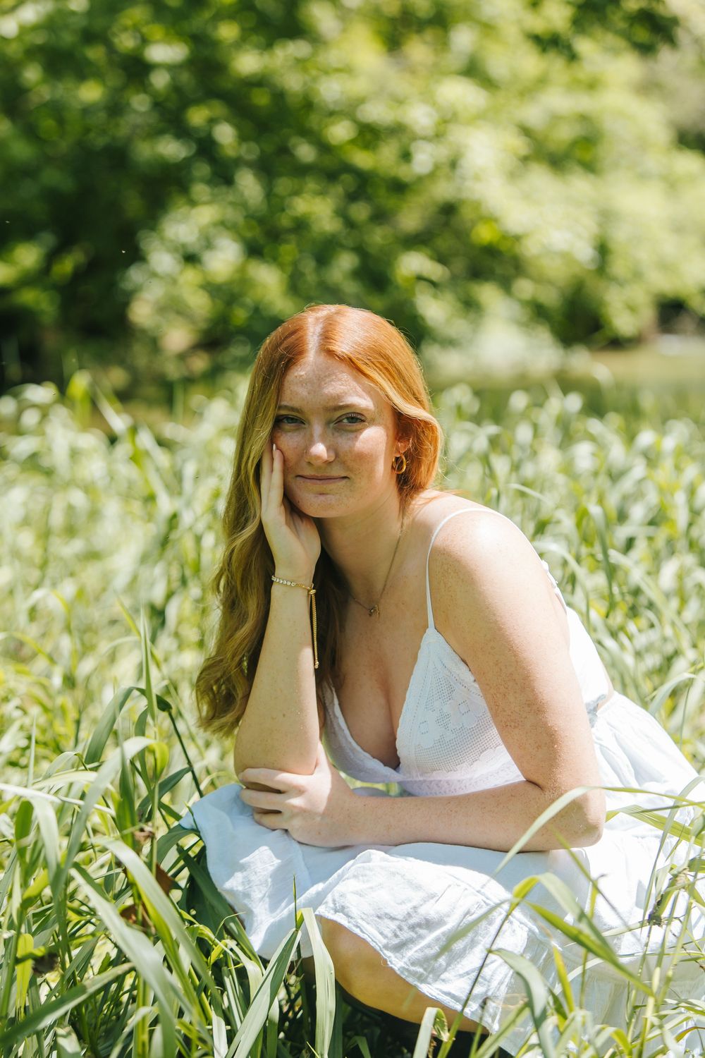 Red-haired woman in white dress sitting peacefully in lush green field on a sunny day.