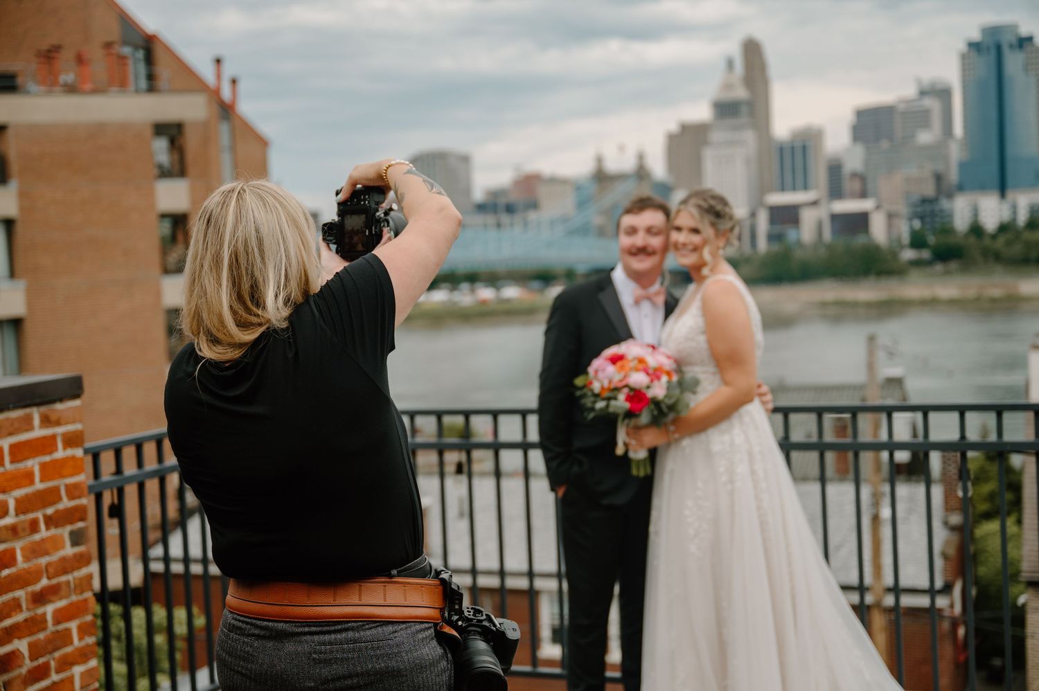 Wedding photographer capturing bride and groom portraits on a rooftop deck with city skyline and river in the background by Kristina Herman