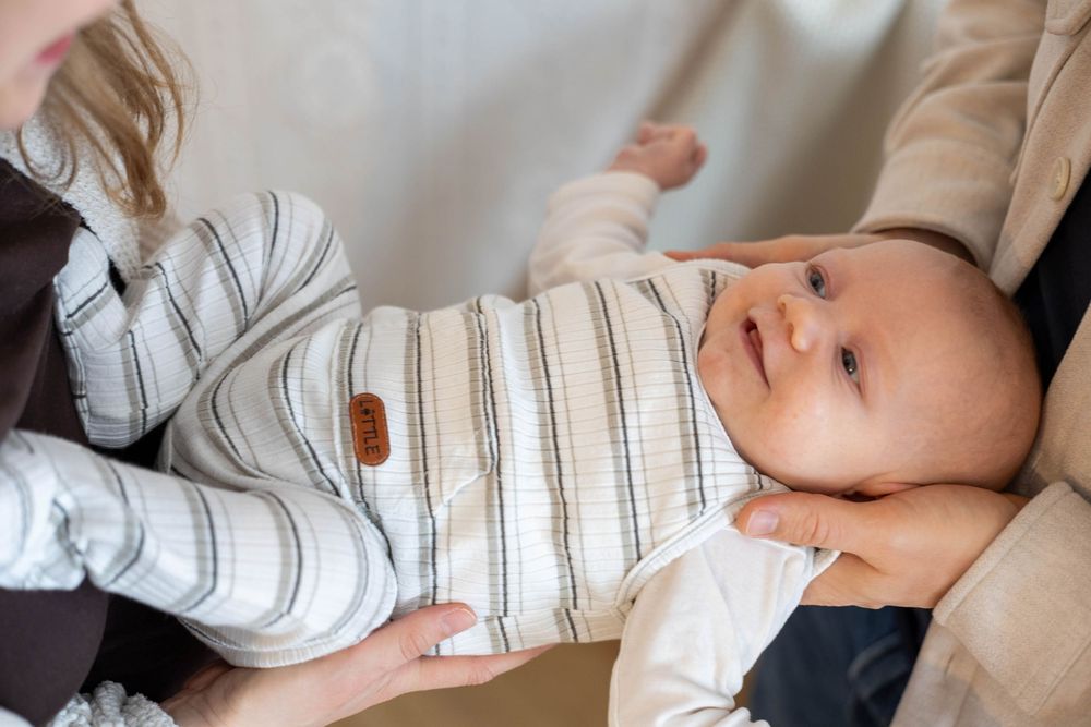 Newborn baby in striped onesie being held by parents, looking alert and calm.