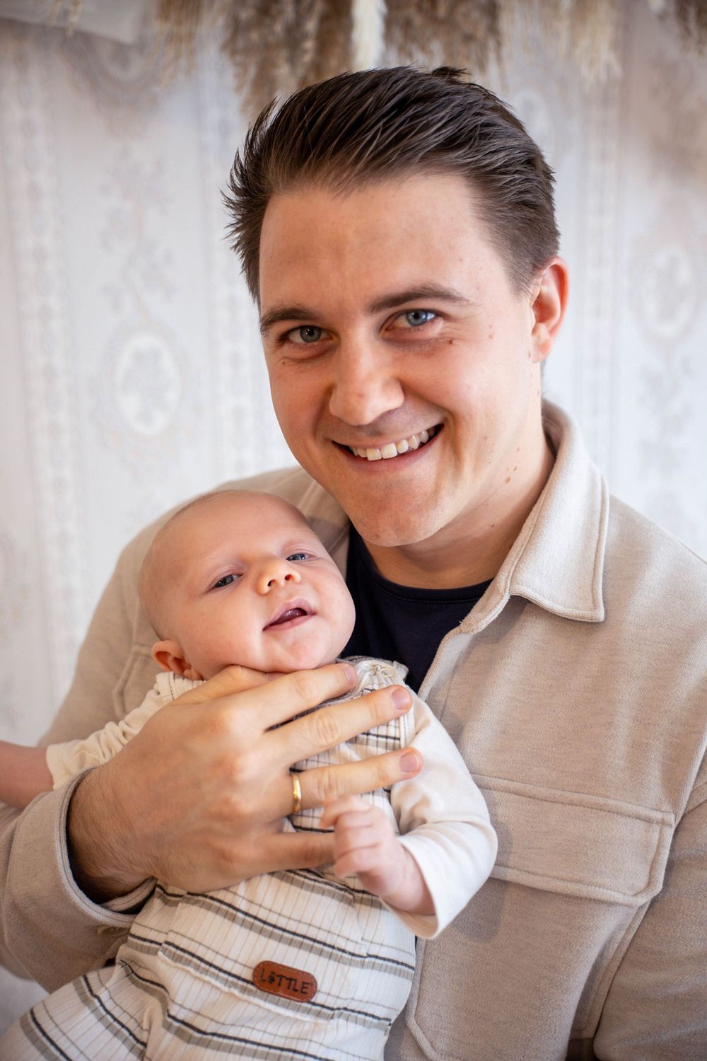 Smiling young man with blue eyes holding a happy baby infant, portrait photo indoors.
