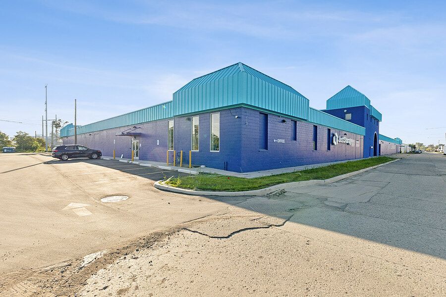Exterior corner view of a purple brick and teal metal commercial storage building with parking lot.