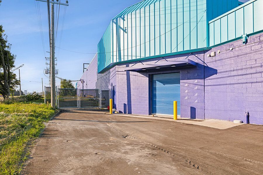 Loading dock area of purple brick storage facility with teal metal siding, blue door, and yellow bollards.