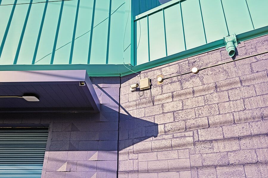 Teal metal roof and gray concrete block wall with security cameras mounted outside a commercial building.