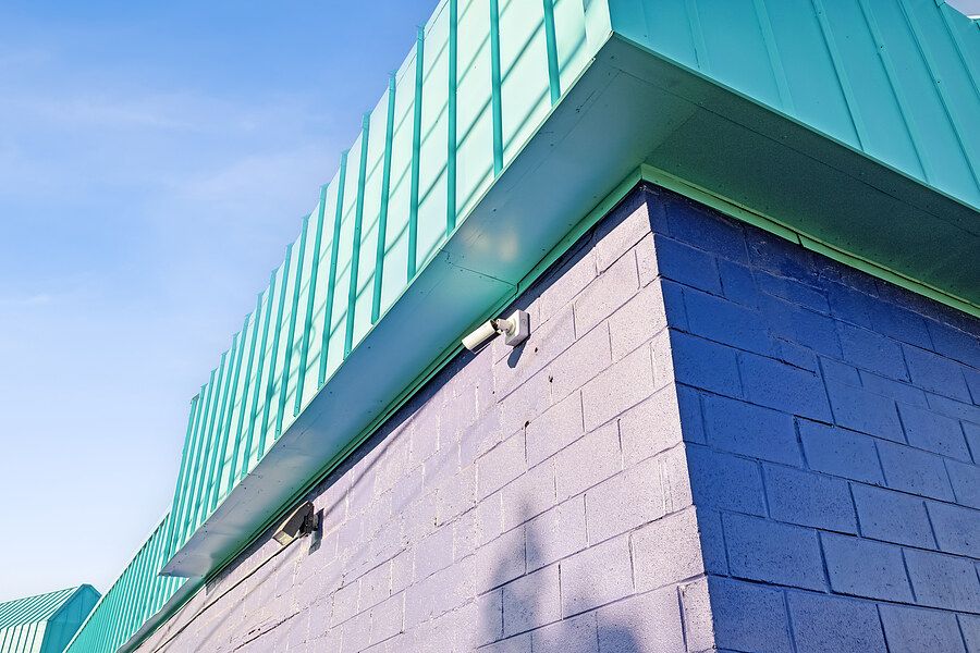 Close-up of a commercial building exterior featuring teal metal roofing and blue concrete block walls under a clear sky.