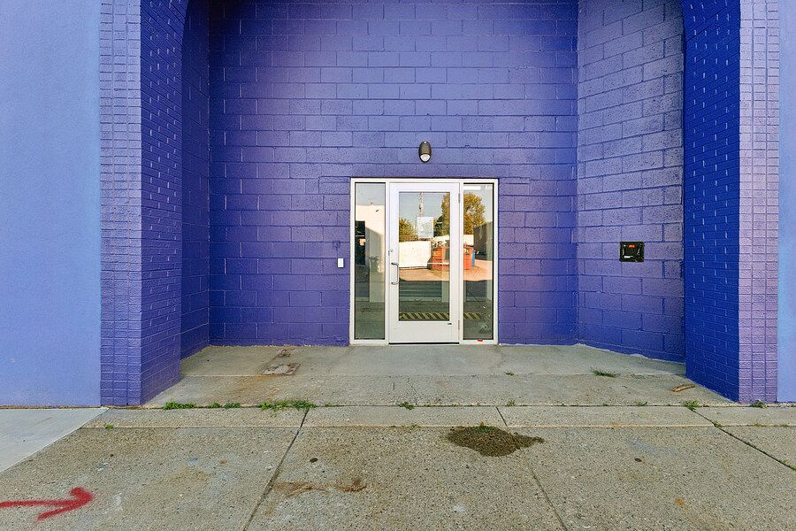 Purple brick building exterior with glass double doors entrance and concrete sidewalk.