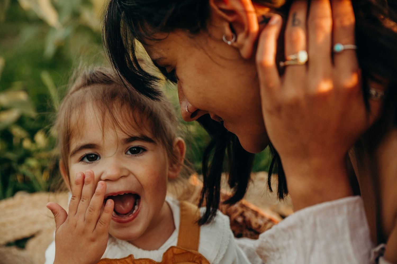 Laughing toddler girl and mother sharing joyful moment outdoors in warm golden light.