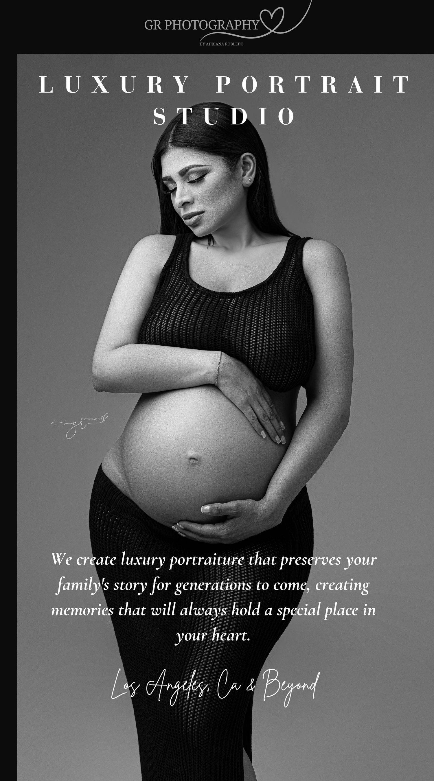 Black and white maternity portrait of a pregnant woman in a dark dress cradling her baby bump at a luxury portrait studio.