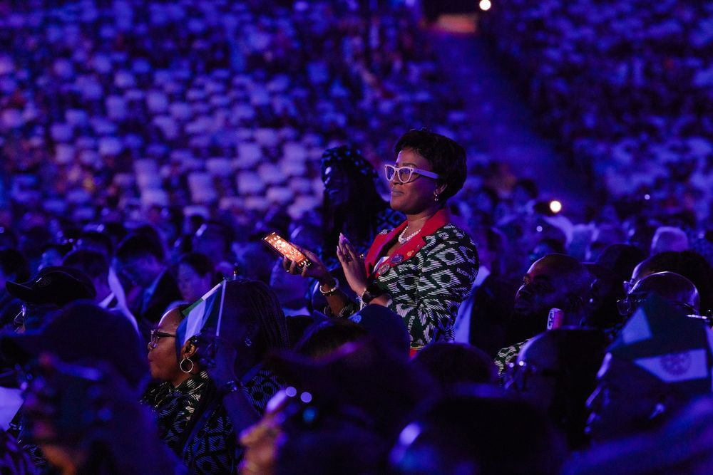 Woman in colorful attire clapping and enjoying a large-scale indoor event or concert.