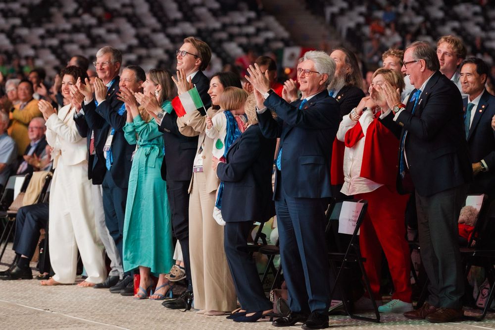 A group of elegantly dressed dignitaries and officials applauding together at a formal ceremony or event.