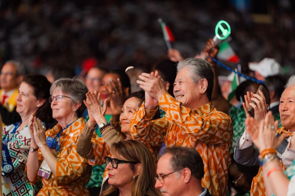 Diverse attendees in matching orange patterned shirts clap and celebrate at a large international gathering.