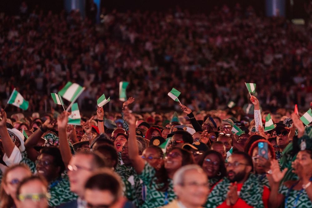 Large crowd waving small green and white flags at an international gathering or convention.