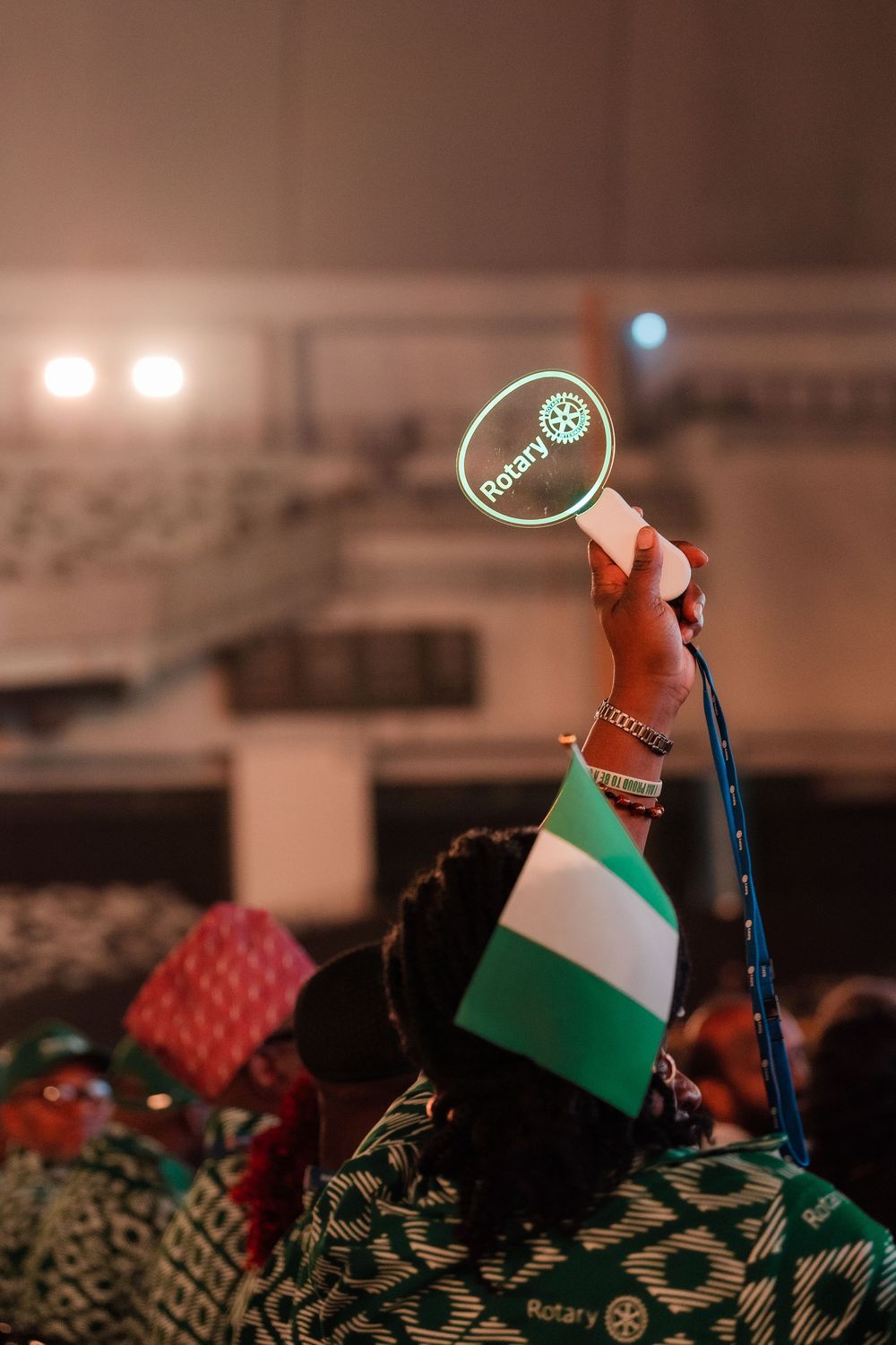 Hand holding illuminated Rotary International sign with Nigerian flag at a conference event.