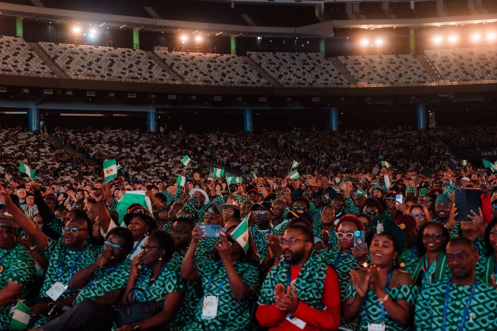 Large crowd of diverse attendees waving green flags at an international Rotary convention inside a stadium.