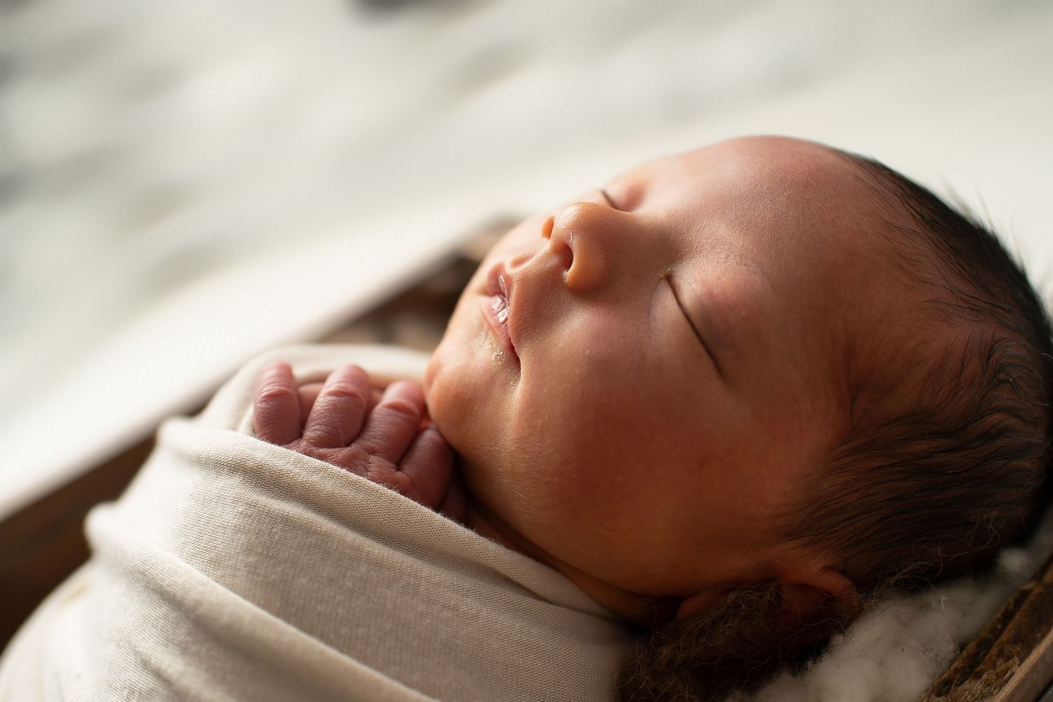 Serene newborn baby swaddled in a white wrap, sleeping peacefully in a warm natural light setting.