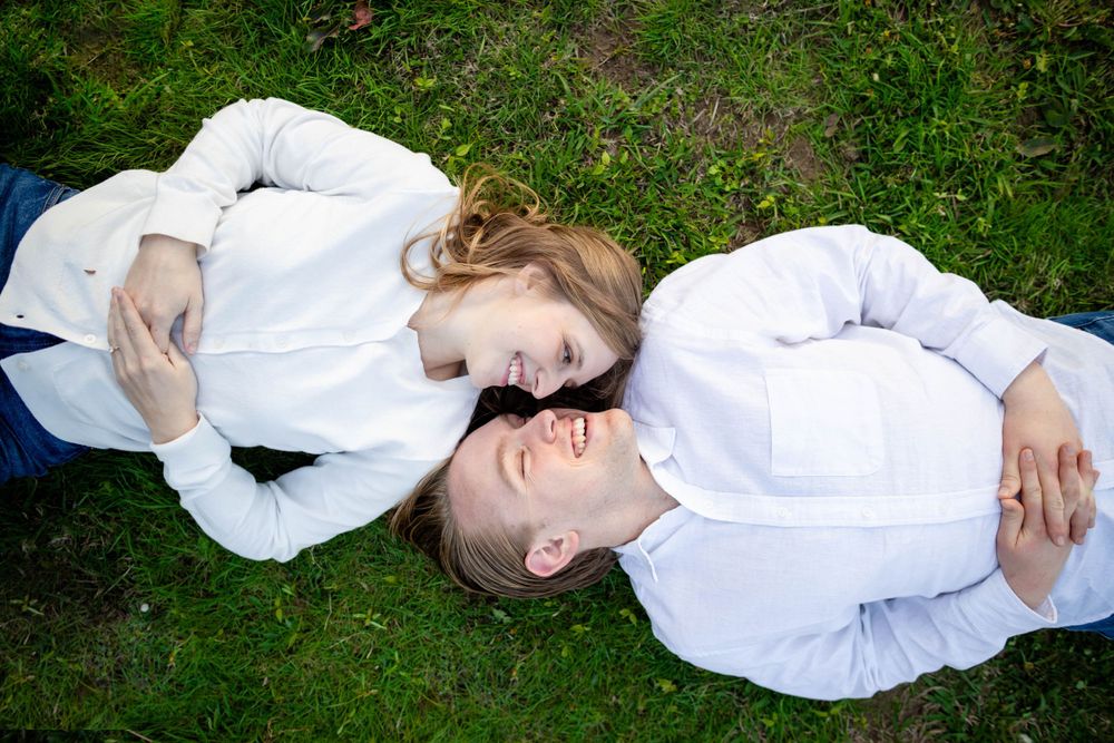 Couple dressed in white lying in the grass with heads together at an outdoor couples session near the Buffalo River