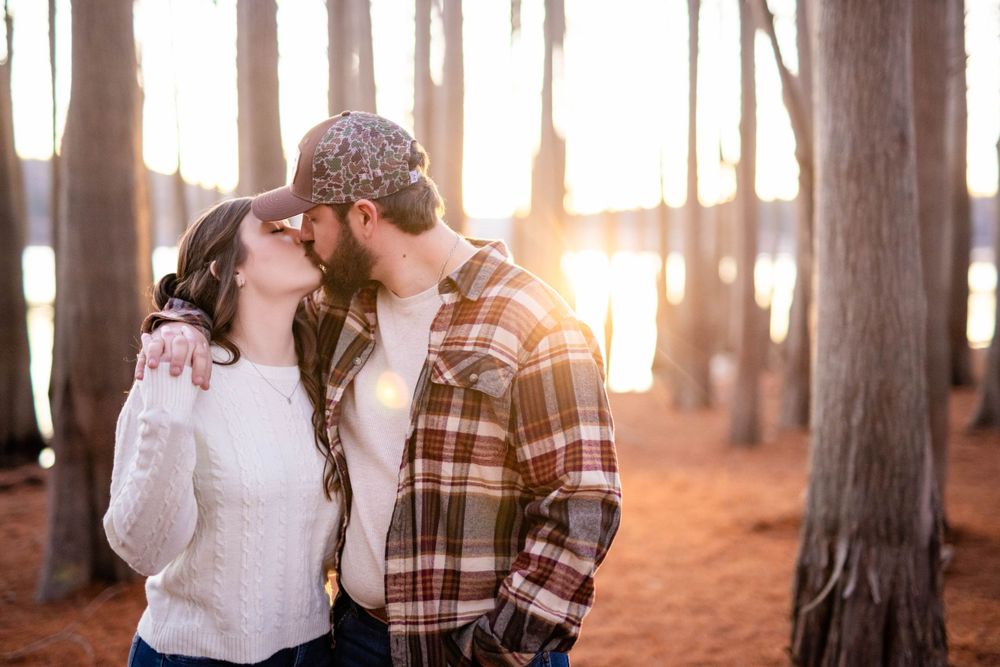 Couple kissing among tall trees in golden light during a couples session at Lake Norfork in Mountain Home, Arkansas