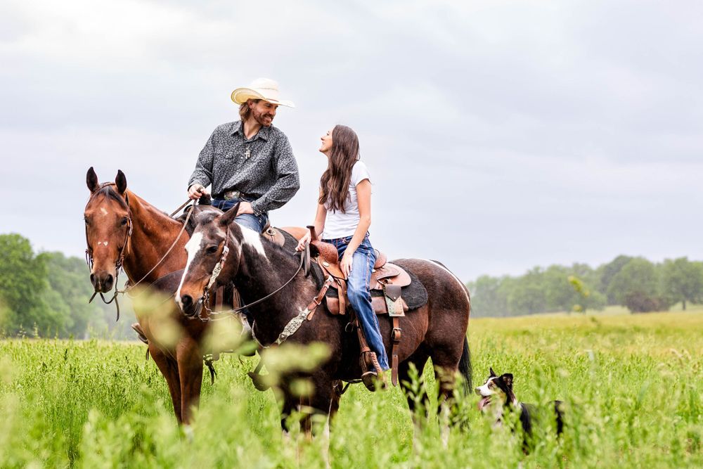 Couple in cowboy hats riding a horse together through a grassy field during a Western couples session in Mountain Home, Arkansas