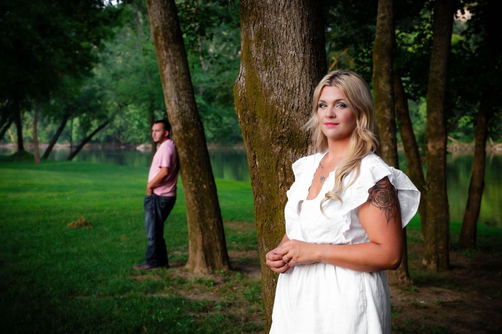 Woman in a white dress leaning against a tree with her partner behind her during a couples session near the Buffalo River