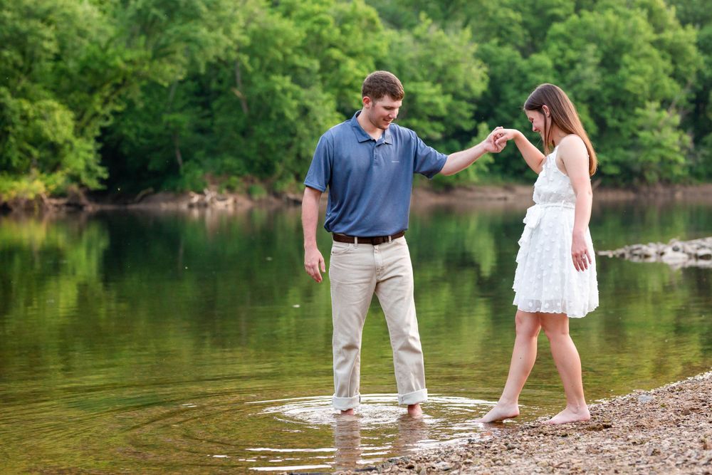 Couple holding hands at the edge of the water on a wooded riverbank during a couples session near the Buffalo River