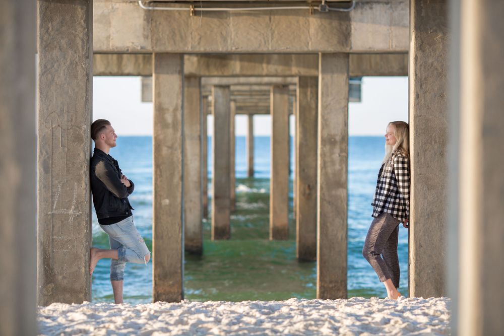 Couple framed beneath a pier with the ocean behind them during a beach couples session at Orange Beach, Alabama