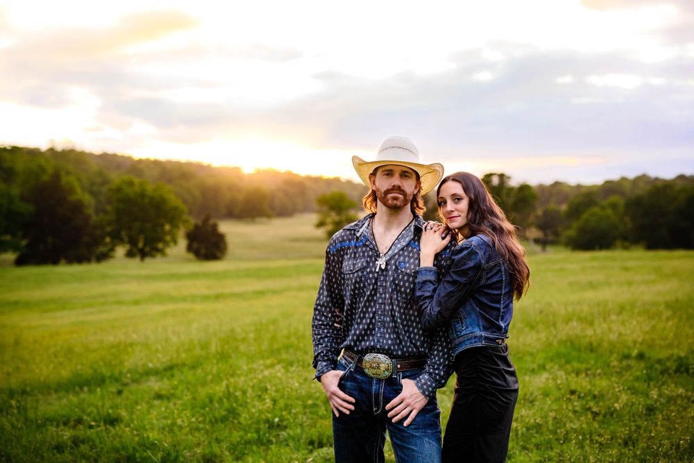 Couple in Western wear standing in an open field at golden hour during a couples session in Mountain Home, Arkansas