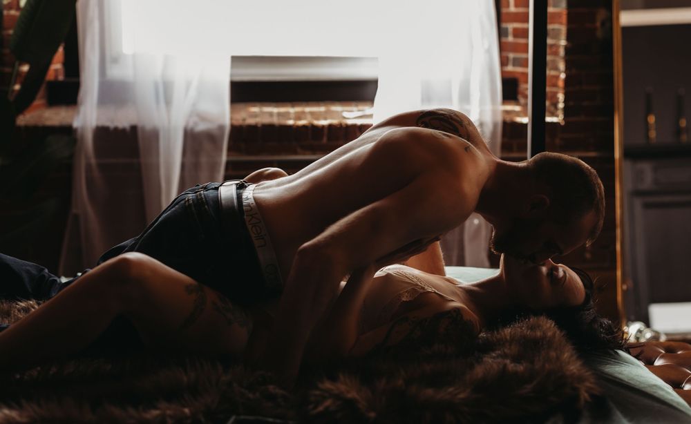 Romantic couple sharing an intimate kiss while lying together in a warmly lit, moody bedroom setting.